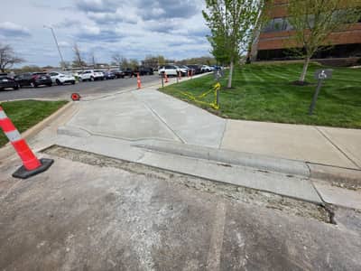 New concrete sidewalk and accessible curb ramp beside an office building parking lot