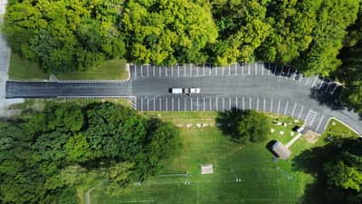 Aerial view of a newly paved asphalt access drive and parking area surrounded by trees