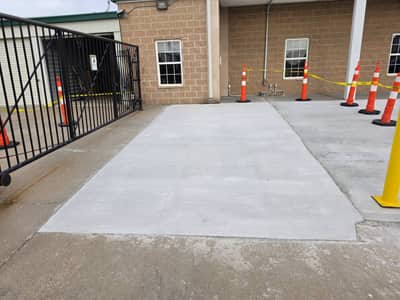 New concrete slab poured at a gated facility entrance, coned off while curing